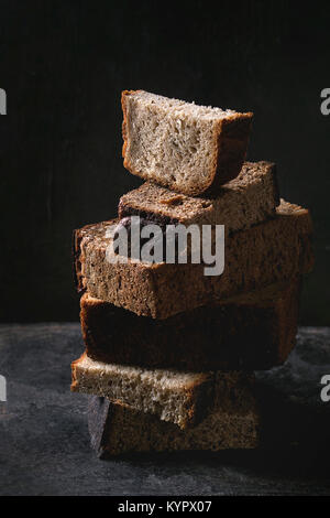 Varietà di pani fatti in casa a fette di pane di segale grano intero e i semi in pila sul vecchio sfondo scuro. Close up. Mangiare sano Foto Stock