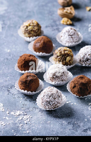 Varietà di fatti in casa tartufi di cioccolato fondente con polvere di cacao, noci di cocco, noci sopra blu sullo sfondo di texture. Close up con lo spazio. Foto Stock