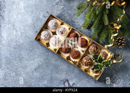 Varietà di fatti in casa tartufi di cioccolato fondente con polvere di cacao, noci di cocco, noci come regalo di Natale nella scatola dorata con abete, decorazioni di Natale un Foto Stock