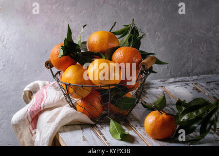 Mature clementine organici o i tangerini con foglie in cesto in piedi con carta asciugatutto su bianco tavolato in legno tavolo con muro grigio come sfondo. Rus Foto Stock