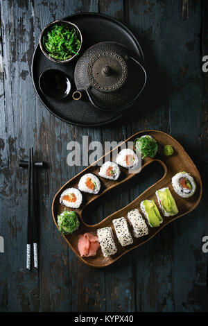 In casa sushi set di rulli con salmone, i semi di sesamo e avocado servire nel piatto di legno di rosa di zenzero sott'aceto, la salsa di soia, wasabi, insalata di alghe marine, costolette Foto Stock