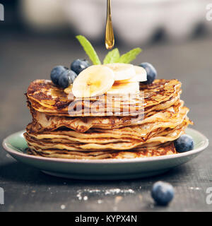 Torre di pancake con banane fresche, mirtilli e miele su un tavolo rustico Foto Stock