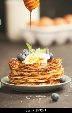 Torre di pancake con banane fresche, mirtilli e miele su un tavolo rustico Foto Stock