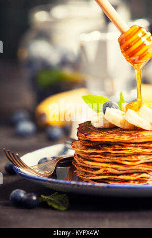 Torre di pancake con banane fresche, mirtilli e miele su un tavolo rustico Foto Stock