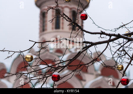 Rami di albero decorato con rosso e giallo di ornamento in vetro le sfere e le luci, storica chiesa edificio in background, cielo nuvoloso Foto Stock