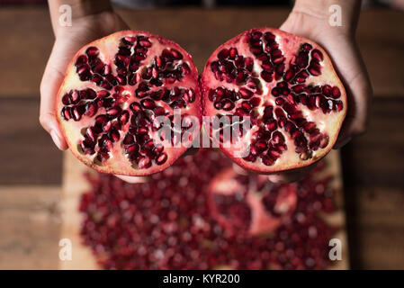 La mano che mostra un taglio melograno frutti sui semi di melograno sfondo Foto Stock