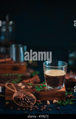 Colpo Espresso con schiuma su una scatola di legno con i chicchi di caffè arabica, foglie, cannella e spezie su sfondo scuro. La preparazione del caffè nella stampa francese. Foto Stock