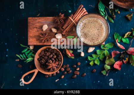 Piatto con laici colpo espresso con schiuma su una scatola di legno, i chicchi di caffè arabica, foglie, cannella e spezie su sfondo scuro. Bevanda calda con fotografia Foto Stock