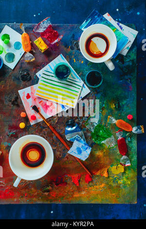 Artista workplace vuote con tazze di caffè, olio e acquerello pennelli per dipingere su una tavolozza colorata, schizzi e spuntini. Lay piatto con copia spazio. Win Foto Stock