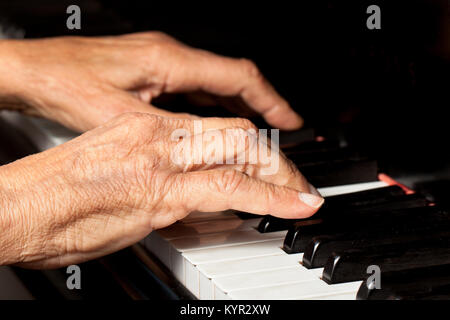 Vecchie mani suonare il pianoforte. In prossimità delle dita e tasti di pianoforte su sfondo nero. Copia dello spazio. Foto Stock