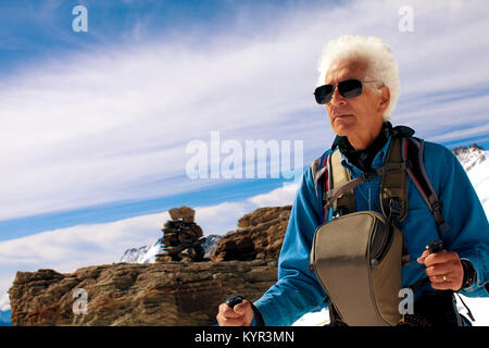 Senior uomo trekking in montagna su viaggi avventura viaggio per le Alpi svizzere. Indossando occhiali da sole, camera bag bastoncini da trekking. Copia dello spazio. Foto Stock