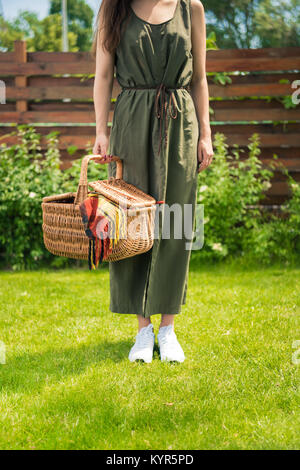 Ritagliato colpo di giovane donna azienda Cesto picnic con plaid mentre si sta in piedi sul prato verde Foto Stock