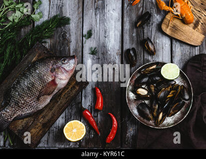 Vista superiore del pesce crudo sul tagliere e cozze con calce su tavola in legno rustico Foto Stock