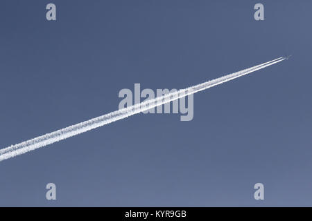 Jet volare attraverso il cielo blu lasciando una scia di vapore o contrail dietro di esso. Foto Stock