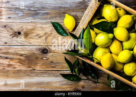 Casella di giallo dei limoni con limone fresco foglie sul vecchio sfondo di  legno con copia spazio. Vista superiore Foto stock - Alamy