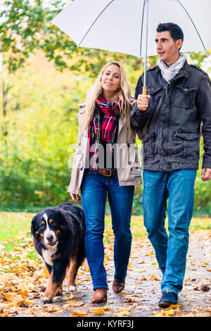 Donna e uomo avente la passeggiata con il cane in autunno la pioggia Foto Stock