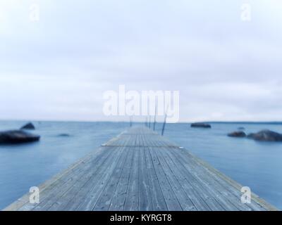 Bagnato dal molo di legno in acqua liscia di Baia Mare. Vecchio mole ancorati con pali di acciaio nella parte inferiore. Scala di Ferro per i passeggeri e i nuotatori. Scheda sfocata essere Foto Stock