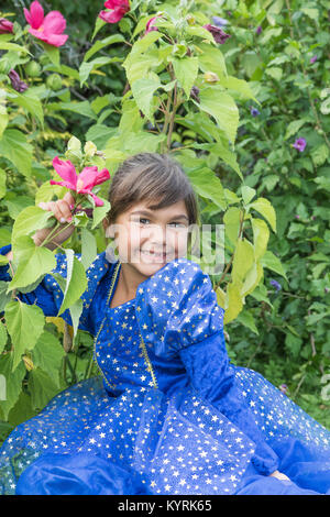 Ritratto di carino sorridente bambina in posa di blu vestiti a fioritura di fiori di ibisco. Foto Stock