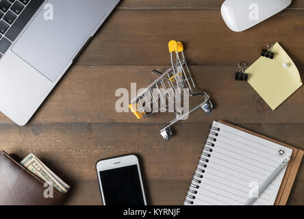 Carrello con laptop e carta bianca su sfondo legno, shopping on-line concept Foto Stock