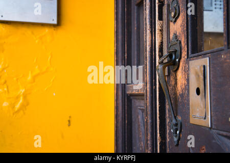 Un vecchio scolpita in bronzo maniglia della porta sulla stessa vecchia porta di legno ricoperta con la colorazione scura, in un edificio con pareti gialle e componenti elettronici obsoleti Foto Stock