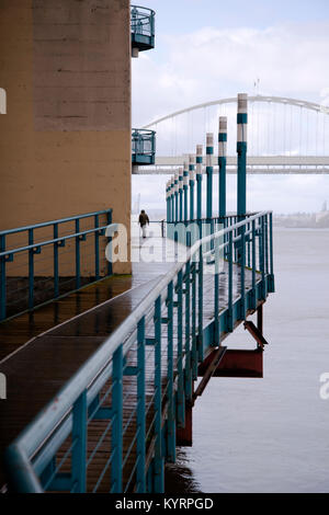 Un uomo cammina lungo il ponte di legno del fiume Willamette in Portland con un recinto e foderato lanterne in piovoso Meteo Portland Foto Stock