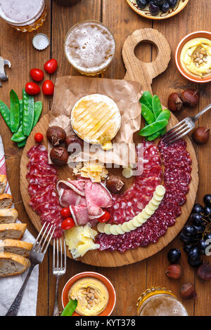 Mix di diversi spuntini e stuzzichini: salsicce, pane, olive, formaggi, castagne, piselli e birra sulla tavola di legno. Vista superiore Foto Stock