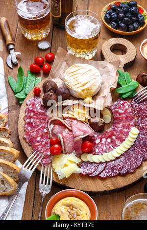 Mix di diversi spuntini e stuzzichini: salsicce, pane, olive, formaggi, castagne, piselli e birra sulla tavola di legno. Vista superiore Foto Stock