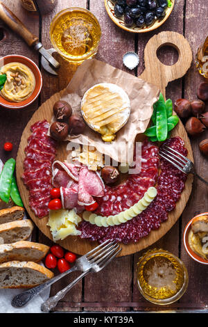 Mix di diversi spuntini e stuzzichini: salsicce, pane, olive, formaggi, castagne, piselli e birra sulla tavola di legno. Vista superiore Foto Stock