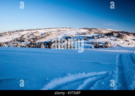 Inverno montagna campagna con insediamento disperso, Tyniok collina con prati e alberi, la neve e il cielo chiaro vicino Koniakow village di Beskid Slaski m Foto Stock