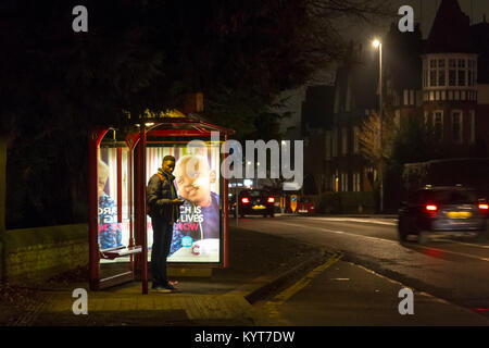 Un giovane maschio in attesa ad una fermata degli autobus in una buia sera inverni di Wellingborough rd, Northampton, Foto Stock