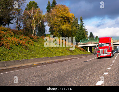 Moderno e di colore rosso brillante big rig semi carrello trattore per carichi su distanze lunghe il trasporto di container sul letto piano semi rimorchio la guida in autostrada road Foto Stock