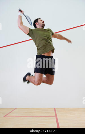 Lettore maschio jumping per colpire una palla durante la partita di squash Foto Stock