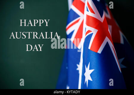 Primo piano di alcuni flag australiano e il testo happy australia giornata contro un sfondo verde scuro Foto Stock