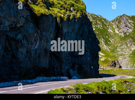 Strada sotto la rupe in alta montagna. Il trasporto con uno sfondo con aspetto pericolose Foto Stock