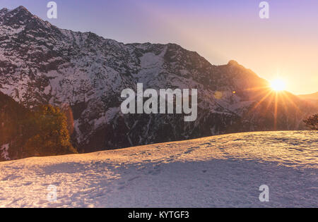 Sole sorge su innevate vette di montagna a Triund, Mcleodganj Dharamsala, Himachal Pradesh, India. Viola/tonalità dorate di Alba. Circondato dalla neve Foto Stock