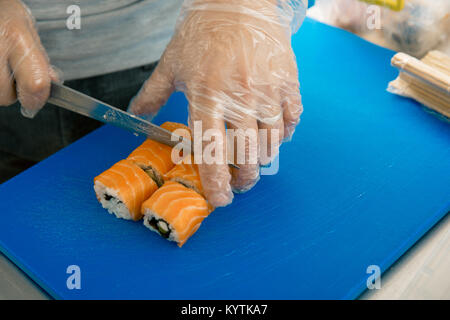 Mano taglia il rotolo closeup su un tagliere. Lo chef prepara il sushi al ristorante giapponese. cookery Foto Stock