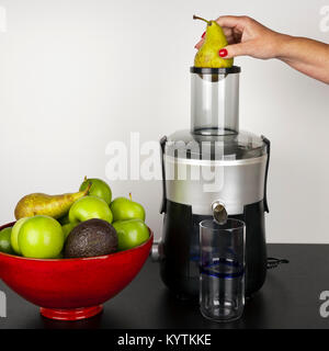 Un womans mano che tiene una pera pronto per cadere in una centrifuga prima di effettuare una frutta e verdura frullati Foto Stock