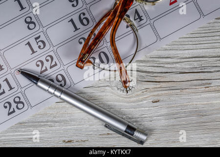 Calendario ,occhiali e penna su sfondo di legno Foto Stock