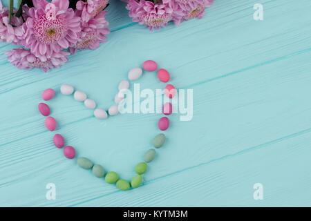 Il cuore da caramelle, copia dello spazio. Cuore realizzato da caramelle colorate e fiori blu su sfondo di legno. Biglietto di auguri per il giorno di San Valentino. Foto Stock