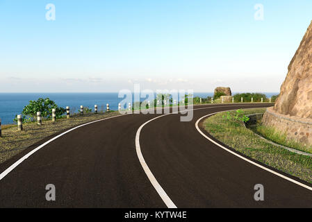 Asfalto strada costiera intorno a bordo scogliera curva, con il mare blu back drop. Foto Stock