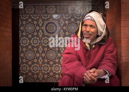 Ritratto di un gentile uomo vecchio guardando nella telecamera seduta in una porta nella Medina di Marrakech, Marocco. Foto Stock