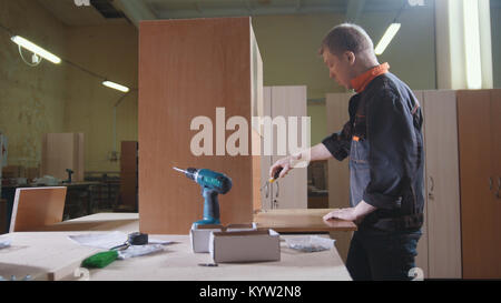 Carpenter lavora con un elettrico cucitrice industriale in fabbrica che fissa i dettagli di mobili Foto Stock