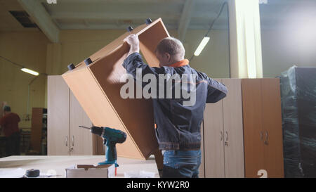 Carpenter lavora con un cacciavite elettrico sul banco di lavoro in fabbrica che fissa i dettagli di mobili Foto Stock