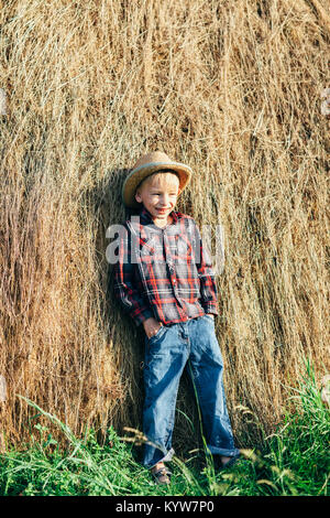 A piena lunghezza Ritratto di ragazzo in posa di lazy farmer, pendente pagliaio. Giovani prankster ponendo sullo sfondo di fieno in campagna all'esterno. Relax Foto Stock