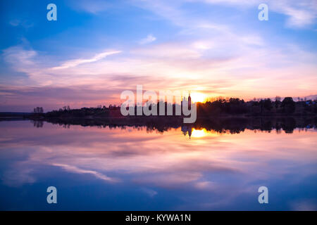 Bellissimo paesaggio rurale con sunrise su fiume. viola le nuvole in cielo si riflette in acqua Foto Stock