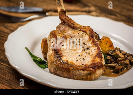 Cotto al forno costolette di maiale o cotoletta con salsa di funghi e patate con spinaci Foto Stock