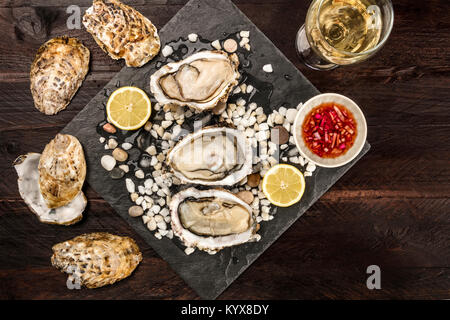 Una foto aerea di appena aperto le ostriche su ghiaccio, con un bicchiere di vino bianco, le fette di limone, salsa vinaigrette e copiare lo spazio, sulla texture scuro Foto Stock