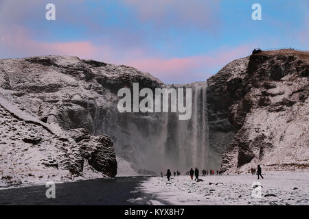 Il 62 metri Skogafoss alta cascata nel sud dell'Islanda come persone ammirano la parte congelati cade. Foto Stock