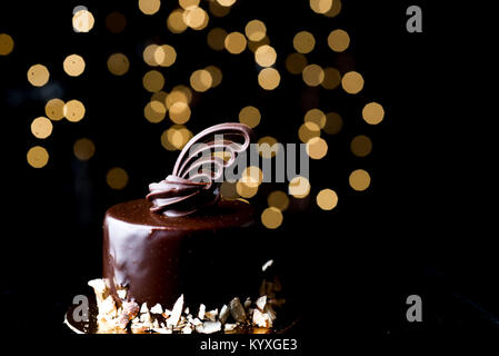 Orizzontale basso studio chiave accesa ganache al cioccolato torte con bordo di mandorle tritate e delicate decorazioni scolpite sulla parte superiore. Bokeh luci soft focus. Foto Stock