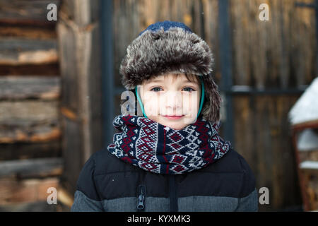 Bel bambino con un dolce sorriso in vestiti caldi contro lo sfondo di legno. Ragazzo vestiti caldi in inverno. Foto Stock